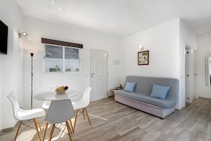 A modern living room with a sofa, dining table, chairs, and a TV.