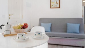 Et hvidt bord med en kaffemaskine, en skål med frugt og to kopper med blomstermønstre.