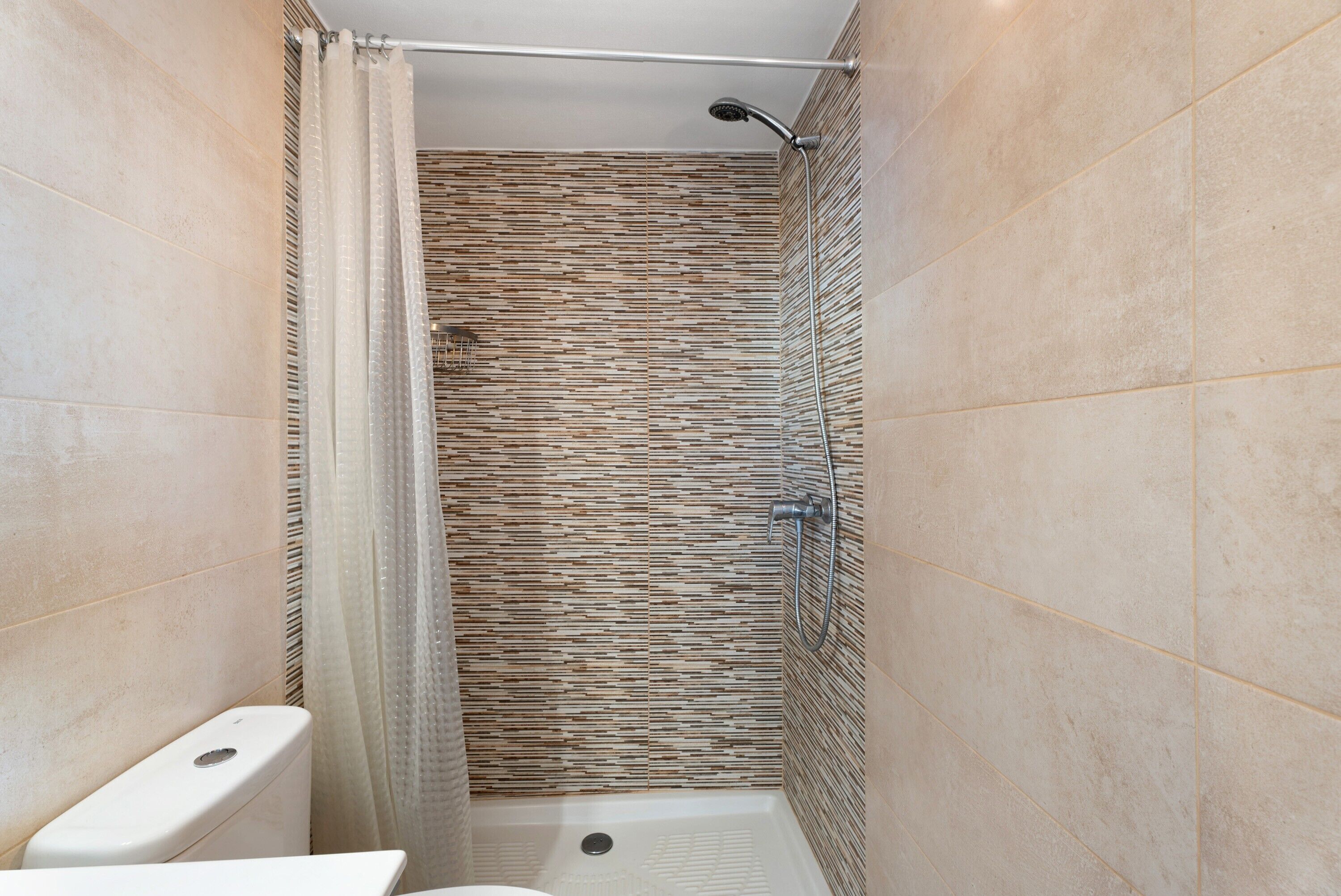 A shower with a glass door, a handheld showerhead, and a tiled wall.