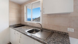 A kitchen with granite countertops, a stainless steel sink, white cabinets, and a window with a view of the sea.