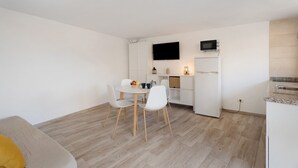 A compact kitchen with a dining area, white cabinetry, a flat-screen TV, and a microwave.
