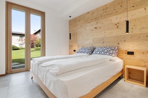 A bedroom with a large bed, wooden headboard, and a view through a sliding door to a garden.