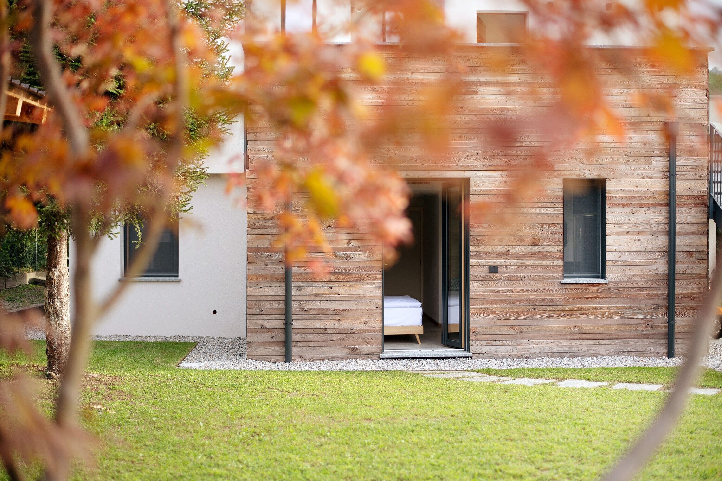 Una casa moderna de madera con un dormitorio visible, un pequeño porche y un césped bien cuidado.