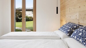Une chambre à coucher avec un lit, une tête de lit en bois et une porte-fenêtre coulissante donnant sur un jardin.