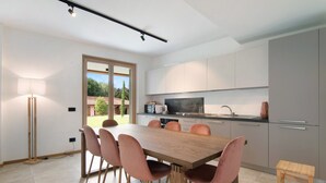 A modern kitchen with a dining area, featuring a large wooden table, pink chairs, and a small wooden stool. - Apartment 'La Villa del Lago in Giardino' with Sea View, Wi-Fi and Air Conditioning (Colico Piano)