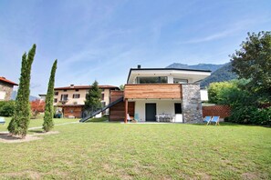 A modern two-story house with a stone facade, a wooden deck, and a view of mountains.