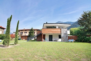 Une maison moderne à deux étages, dotée d’une façade en pierre, d’une terrasse en bois et offrant une vue sur les montagnes.