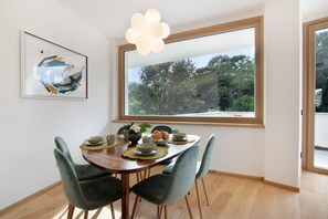 Un coin repas avec une table en bois, quatre chaises, une grande fenêtre et un tableau abstrait encadré.