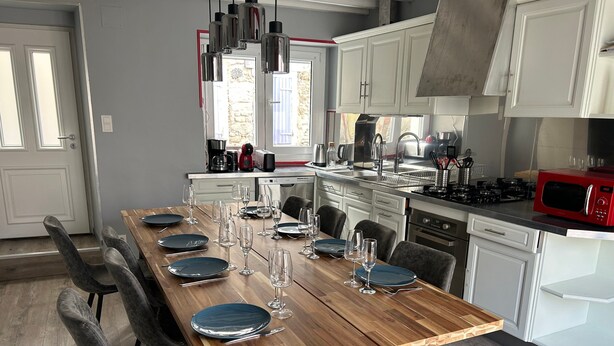 A modern kitchen with a wooden dining table set for six, white cabinets, a red microwave, and a view of a stone building outside. - Holiday Home 'Chez Brigitte' with Private Terrace, Wi-Fi and Air Conditioning (Chatillon sur marne)