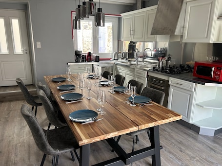 A modern kitchen with a wooden dining table set for six, white cabinets, a red microwave, and a view of a stone building outside.. Holiday Home 'Chez Brigitte' with Private Terrace, Wi-Fi and Air Conditioning