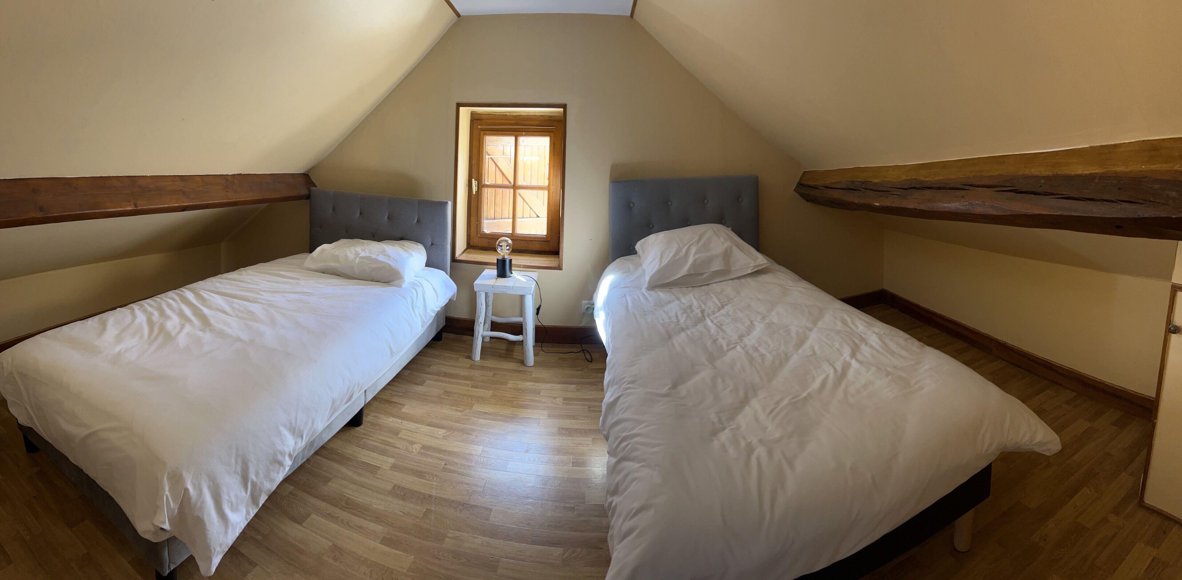 A bedroom with two beds, a small table, and a window.