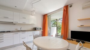 Een moderne keuken met witte kasten, een eettafel, stoelen, een televisie en een balkon met oranje gordijnen.