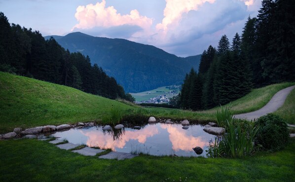 A rural landscape with a pond, grassy hills, and a distant village.