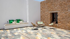 A patio with a stone wall, a white bench with cushions, and wicker chairs. - Casa Rural Berrenda with Sea Views, Private Terrace, and Wi-Fi (Tiscamanita)
