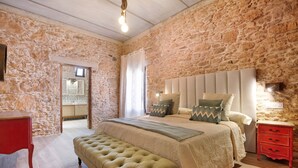A bedroom with a stone wall, a large bed with a headboard, a bench, and a red nightstand. - Casa Rural Berrenda with Sea Views, Private Terrace, and Wi-Fi (Tiscamanita)