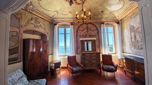 Una stanza con un grande specchio, due poltrone, un divano, un armadio in legno e un soffitto affrescato.