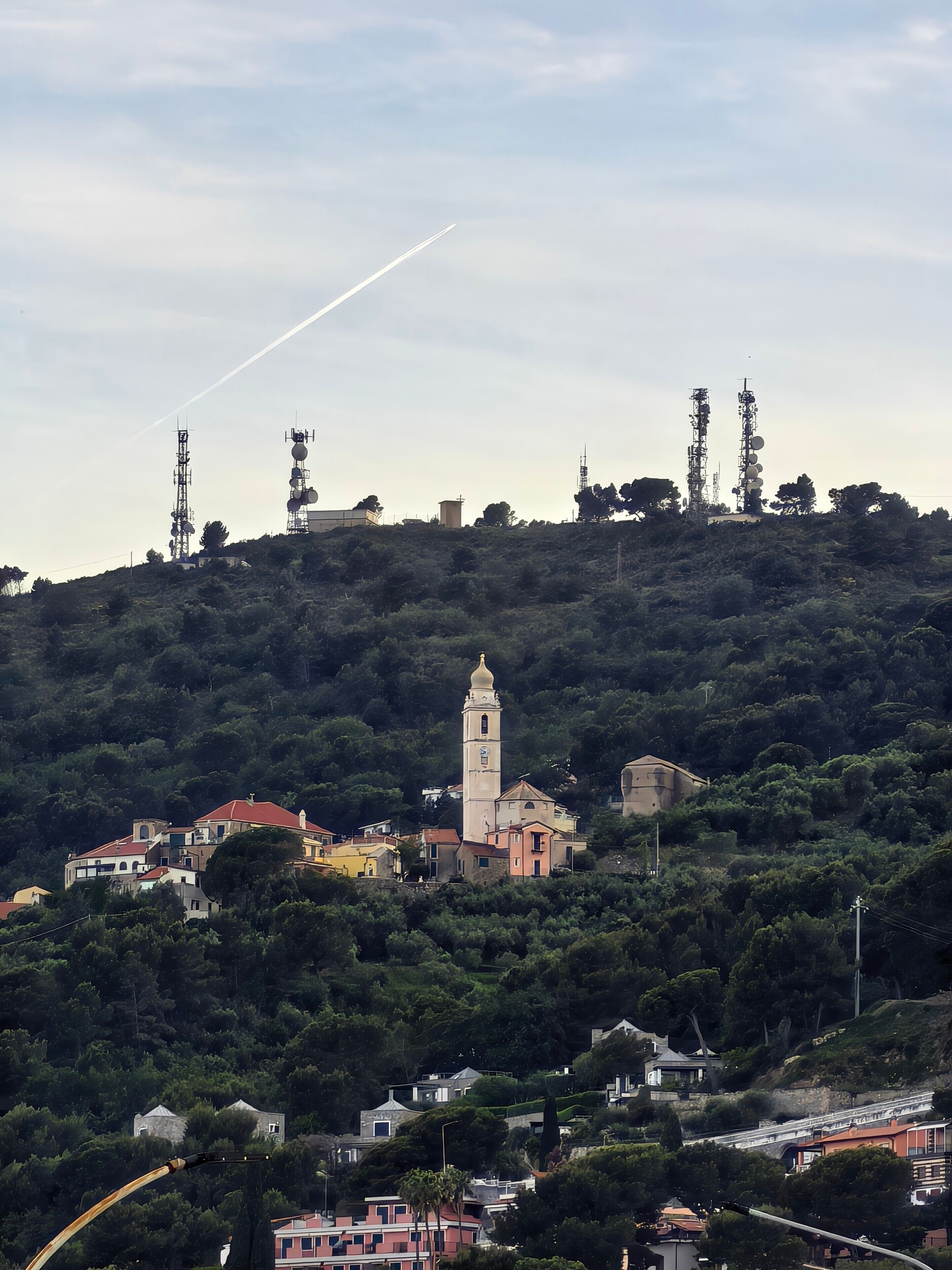 Un pueblo en la ladera de una colina con una imponente torre de iglesia, edificios residenciales y torres de comunicación.