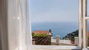Vista attraverso una finestra con tenda, su una zona costiera con edifici e il mare.