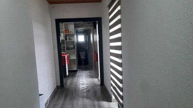 Un couloir avec un plafond en bois, un radiateur et une vue sur une pièce où se trouvent des toilettes et une fenêtre.
