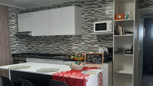 Une cuisine moderne avec un coin bar, des meubles blancs, un four à micro-ondes et une étagère où sont posés des livres et des objets décoratifs.