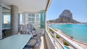 Ein Balkon mit Tisch und Stühlen, Blick aufs Meer und eine markante Felsformation.