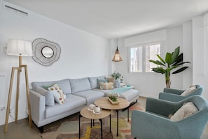 Un salon moderne comprenant un canapé, deux fauteuils, une table basse, une lampe, un miroir et une grande plante.