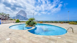 Ein Pool mit geschwungener Form, umgeben von einer gefliesten Terrasse, mit Blick auf einen Berg und das Meer im Hintergrund.