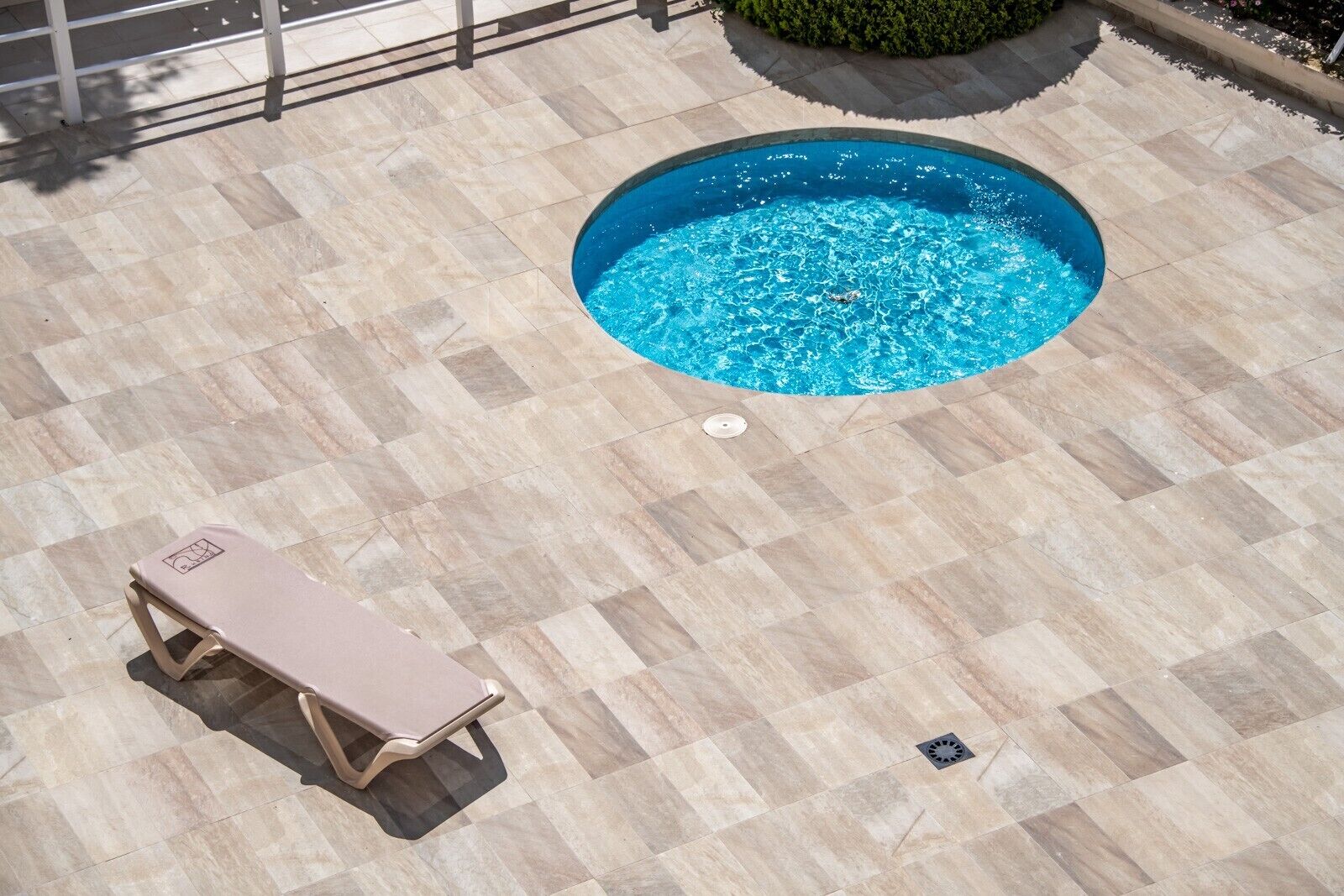 A swimming pool with a tiled deck, a lounge chair, and a small garden area.