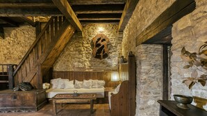 A rustic room with a stone wall, wooden staircase, a white sofa, a wooden table, and a fireplace. - Castle 'Castell De Palau Sator' with Mountain View, Wi-Fi and Air Conditioning (Palau-sator)