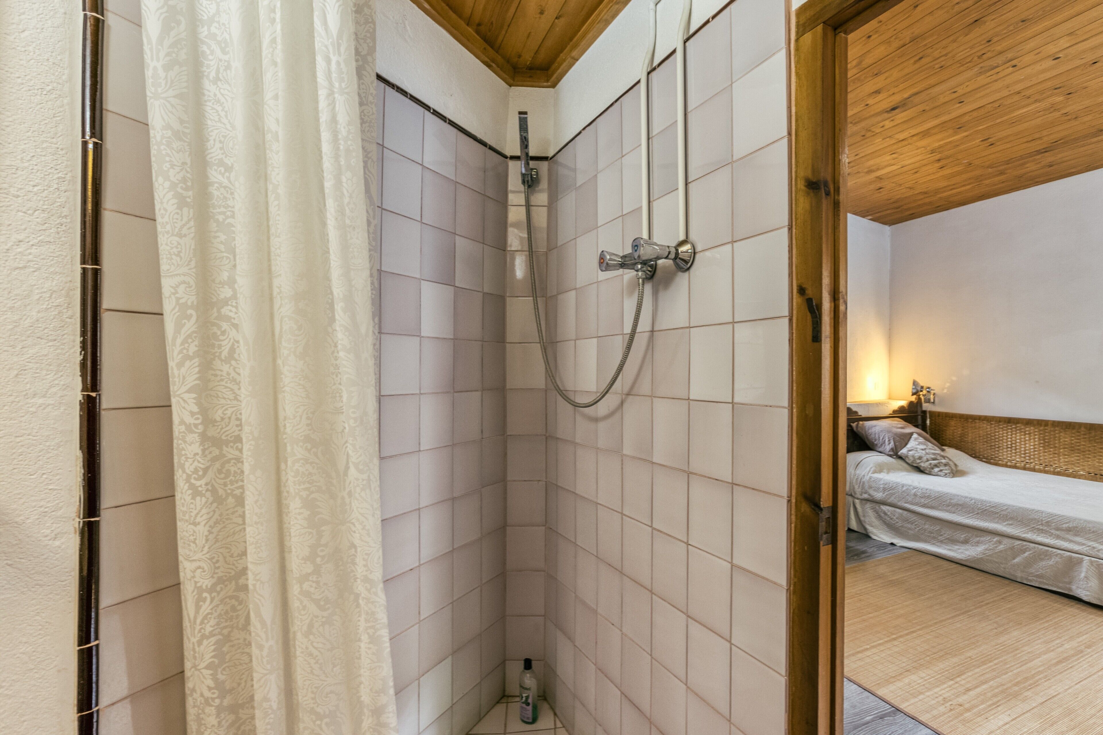 Une petite pièce compacte avec une douche, un lit et un plafond en bois.