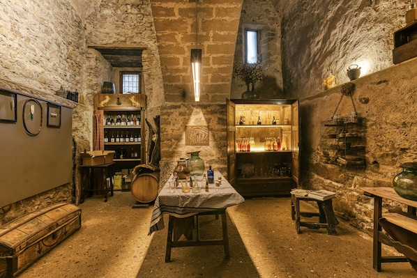 A rustic cellar with stone walls, wooden furniture, and shelves of bottles.