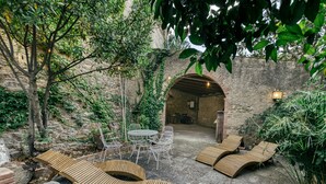 A patio with wooden loungers, a table with chairs, and an arched doorway. - Castle 'Castell De Palau Sator' with Mountain View, Wi-Fi and Air Conditioning (Palau-sator)