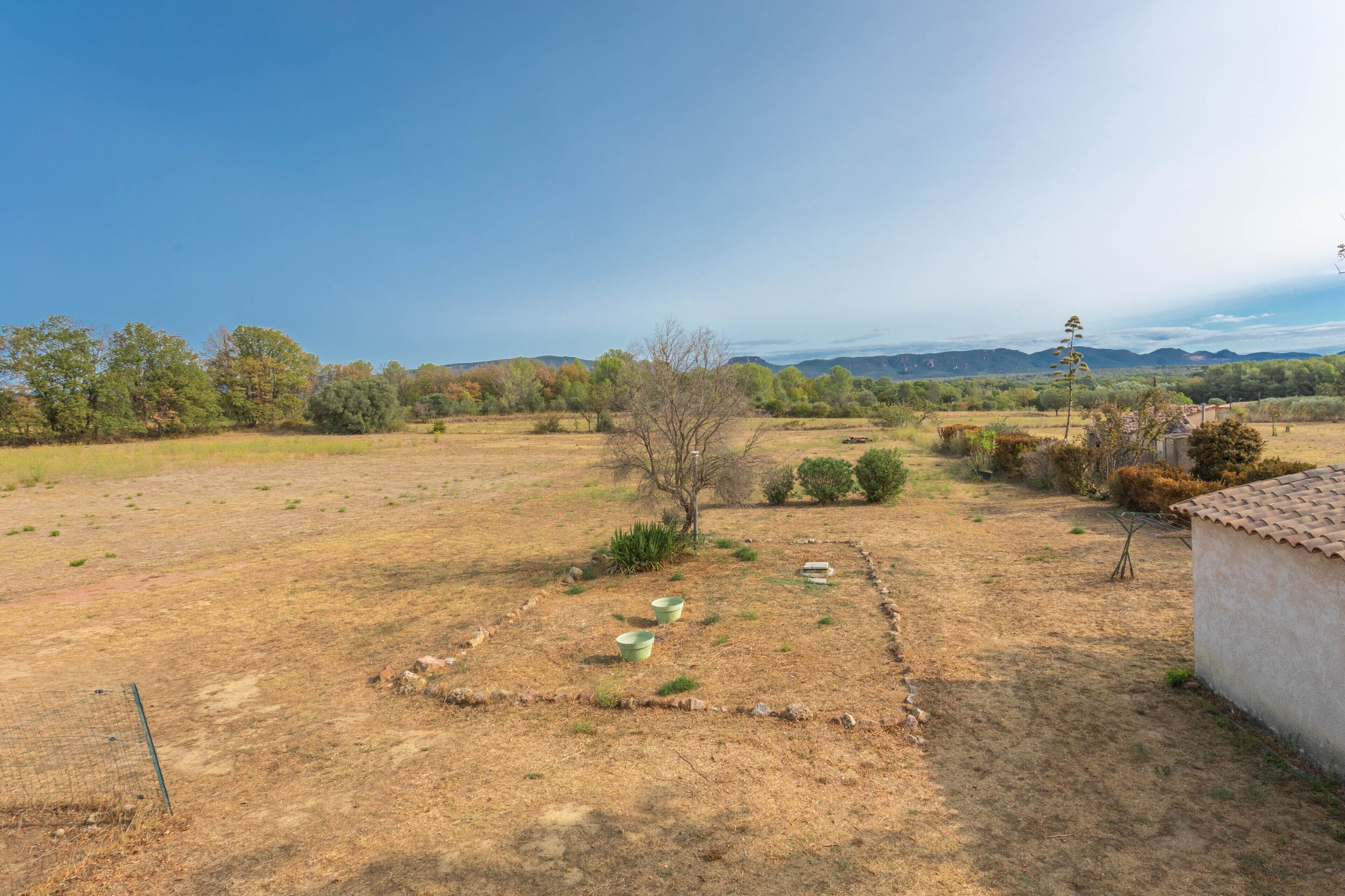 Paesaggio rurale con un recinto, un piccolo edificio e colline in lontananza.