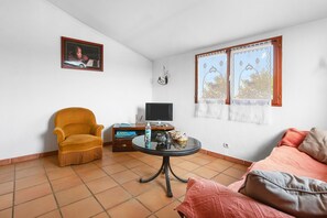 A living room with a sofa, armchair, TV, and a table with a bottle and remote.