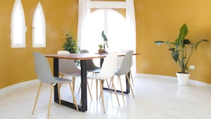 Un coin repas comprenant une table, des chaises, une plante en pot et une fenêtre avec des rideaux.