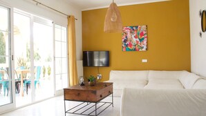 Un salon avec un canapé, un téléviseur, une table basse en bois et un tableau coloré accroché au mur.
