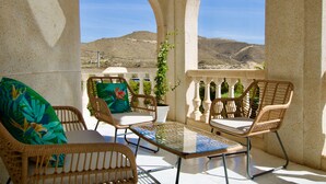 Une terrasse meublée de mobilier en osier, avec une table en verre, et une vue sur un paysage montagneux.