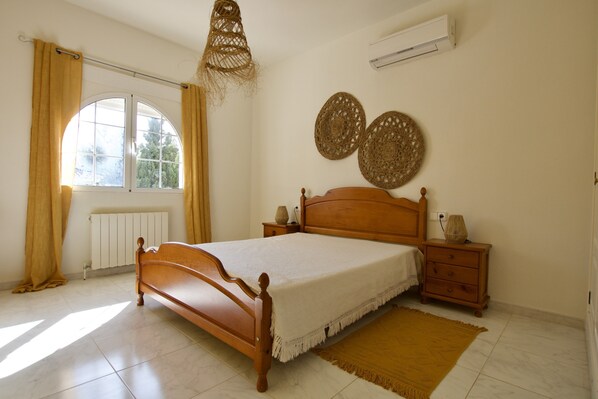 Une chambre avec un lit en bois, une fenêtre avec des rideaux, un radiateur, une table de chevet avec une lampe et deux éléments de décoration murale.
