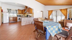 Cozinha com armários de madeira, máquina de lavar e sala de jantar com mesa e cadeiras.