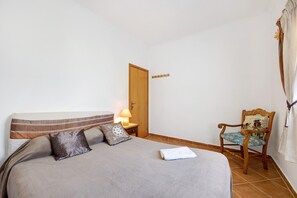 Une chambre à coucher avec un lit, une table de chevet avec une lampe, une chaise en bois et une porte.