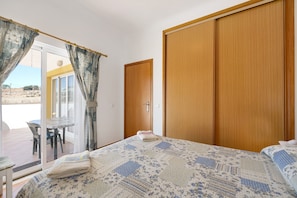 Une chambre à coucher avec un lit, une armoire en bois, une porte et une table avec des chaises à l’extérieur.