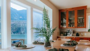 A dining area with a wooden table, leather chairs, and a view of mountains through large windows. - Emerald Haven Lakeside Paradise, Ultimate Retreat (Port Angeles)