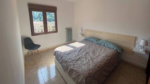 Een slaapkamer met een bed, een stoel, een raam en een radiator.