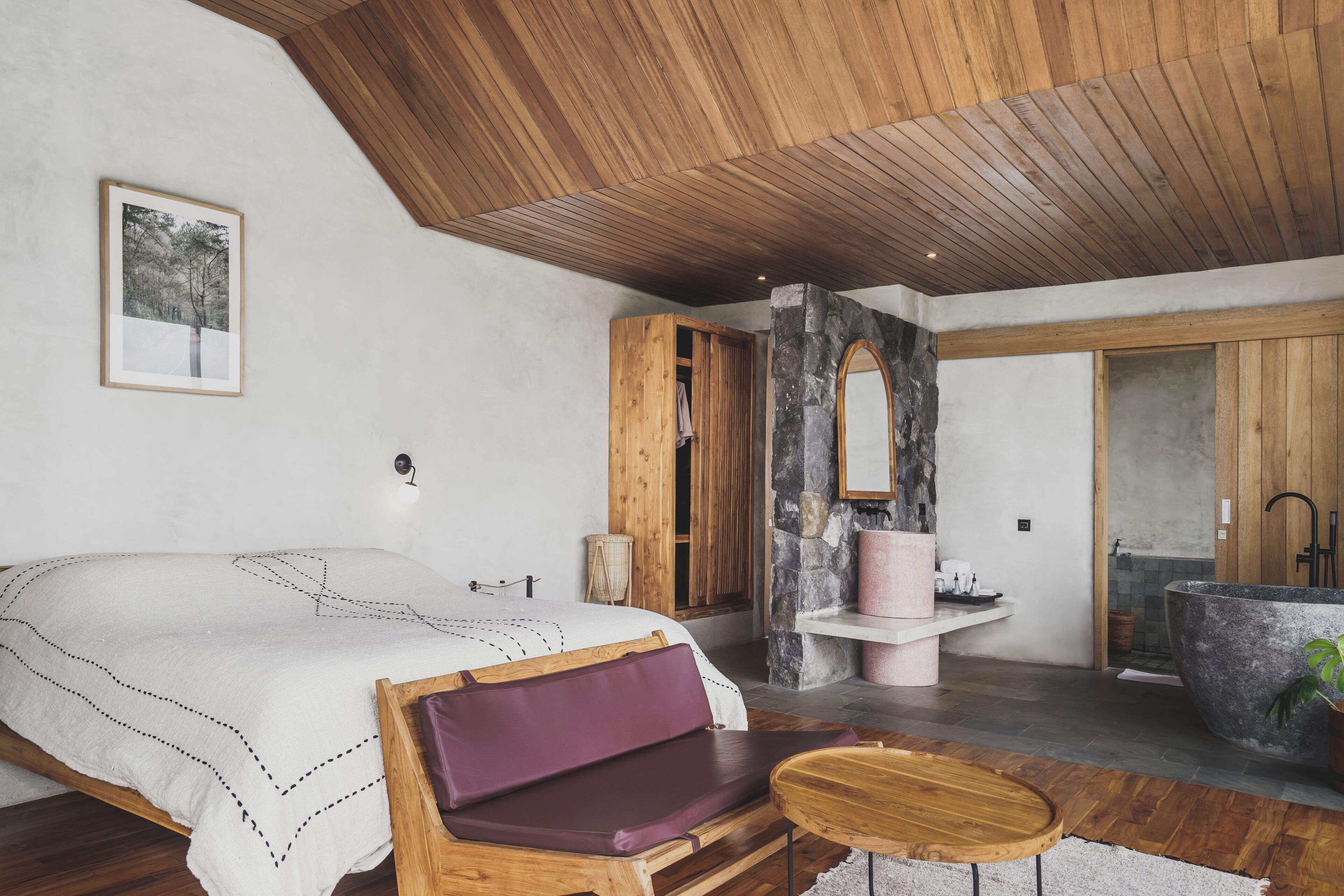 A bedroom with a large bed, wooden furniture, a stone sink, and a bathtub.