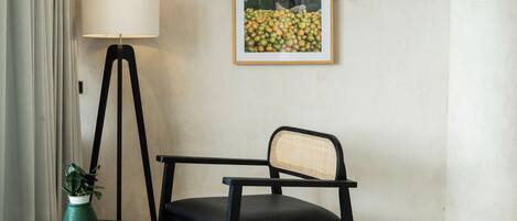 A room with a floor lamp, a framed picture on the wall, a chair, and a potted plant.