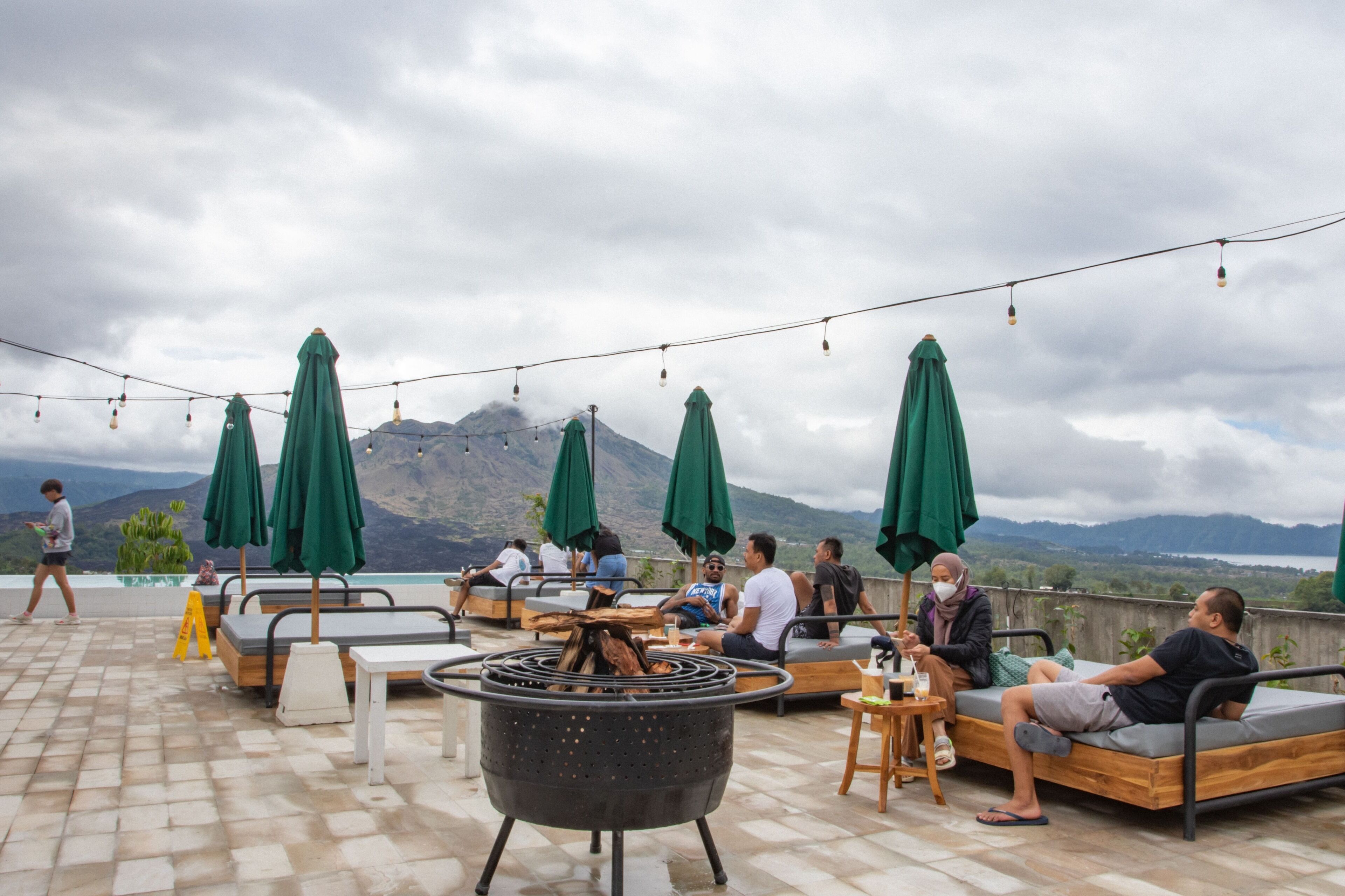 A rooftop terrace with outdoor seating, a fire pit, and umbrellas providing shade.