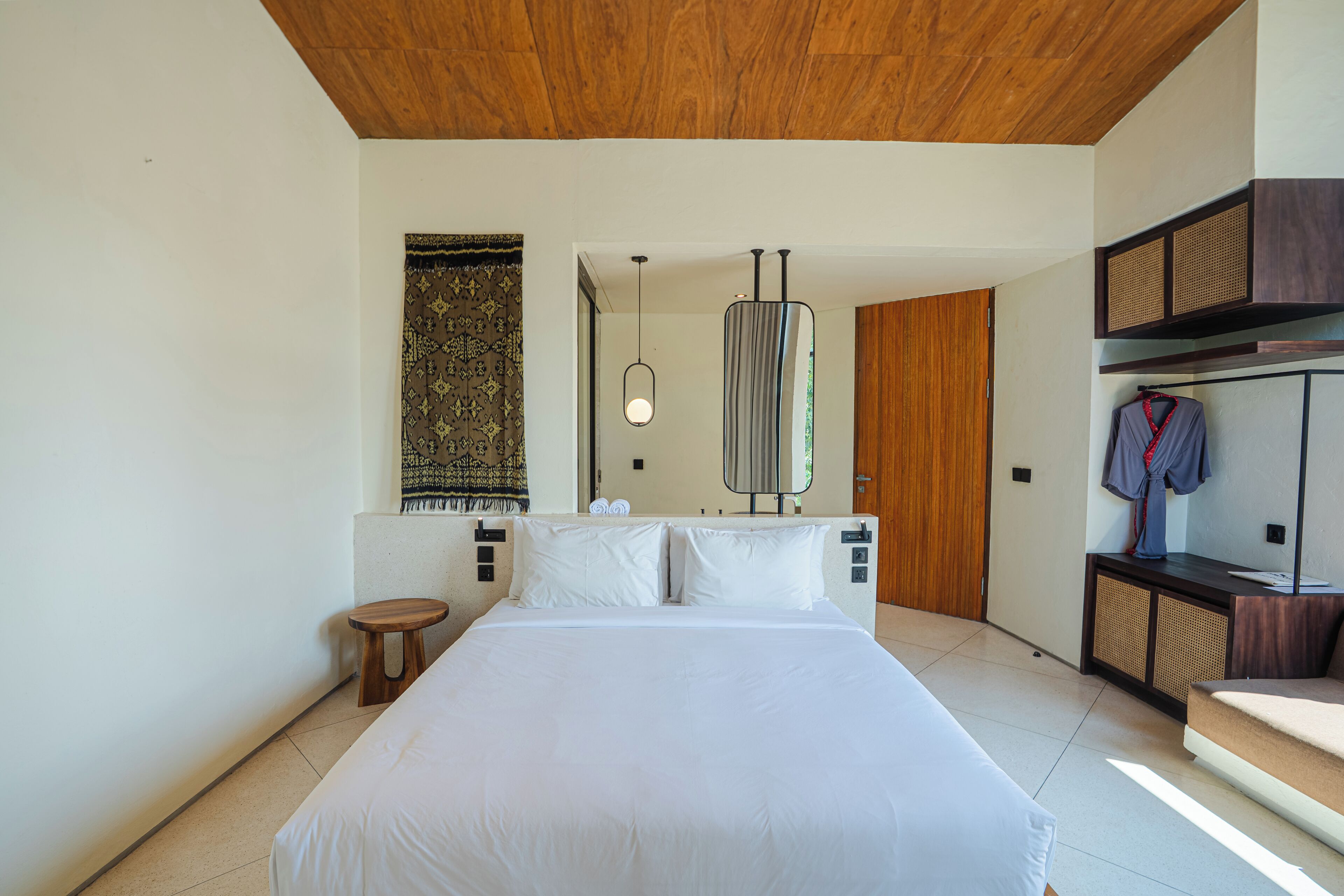 A modern bedroom with a large bed, a wooden ceiling, a hanging light fixture, and a wardrobe with a mirror.