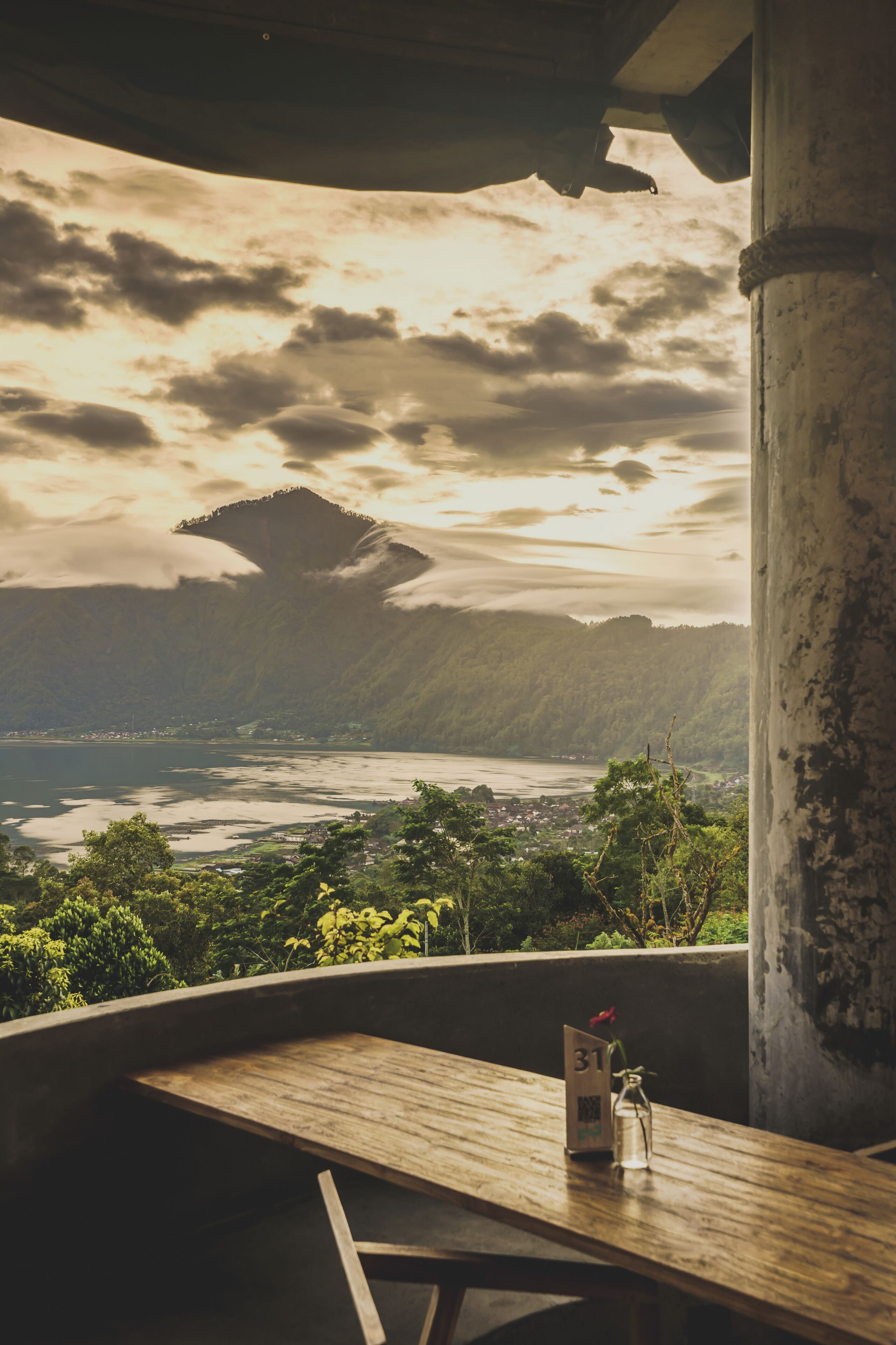 Una mesa de madera con un cartel numerado y una botella de vidrio, con vistas a un paisaje costero con montañas y una masa de agua.