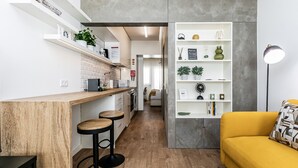 A modern kitchen with a wooden countertop, bar stools, and a yellow sofa. - Apartamento Primavera (Parede)