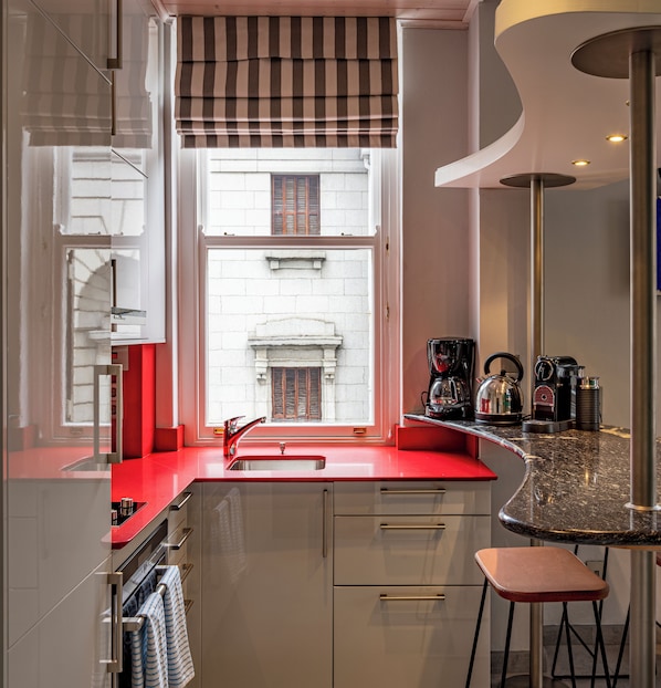 A compact kitchen with a red countertop, a built-in oven, and a window with a view of a building.